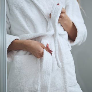 a woman standing in a fluffy white bathrobe she is tying the belt
